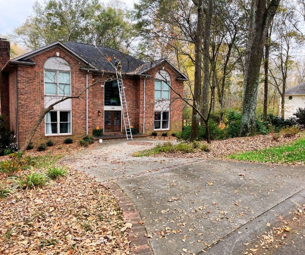 House with brick facade, ladder against roof, and autumn leaves in yard.
